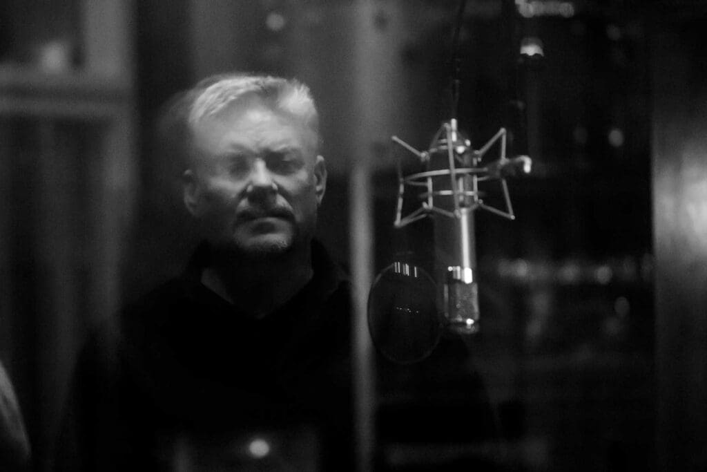 Blurred image of Dan Nachtrab Voice Actor looking through glass at microphone in dark studio